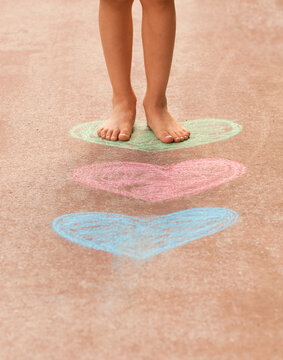Close-up low section of a barefoot boy standing on multi coloured chalk hearts drawn on a pavement
