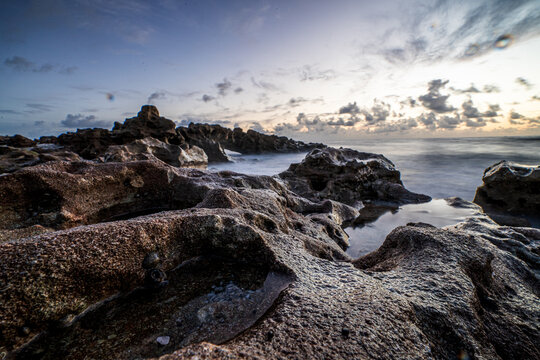 View of a rugged rocky coastline with tide pools and crashing waves under a cloudy sky at dawn in Florida, United States.