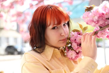 Naklejka premium Beautiful young girl posing near blossoming sakura tree outdoors