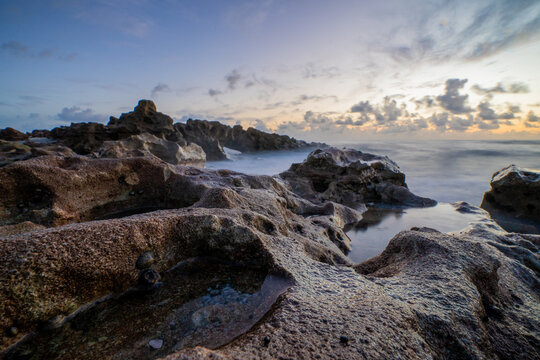 View of rocky coastline with tide pools and ocean waves under a soft morning sky in Florida, United States.