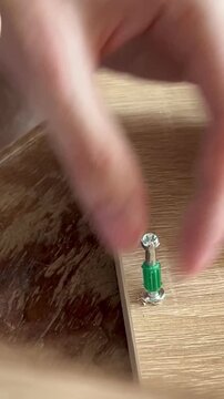 Hand securing a screw with a green anchor into a wooden board, focusing on precision and technique. The action showcases  skills and attention to detail