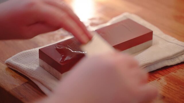 Close up backlit shot of person using a whetstone to sharpen a chef&rsquo;s knife