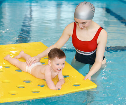 Swimming lesson. Coach teaching little boy to swim with floating mat in pool