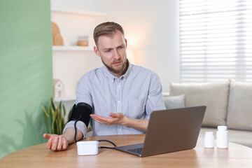 Fototapeta premium Telemedicine. Man measuring blood pressure during online consultation with doctor via laptop at home