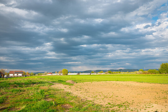 Rural green field under dramatic cloudy sky with distant village and farmland horizon in Mures valley, central Transylvania, Romania.