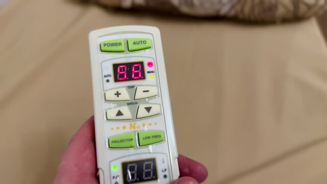 Close-up hand holding remote control adjusting heating temperature on massage bed, LED display changing digits, finger pressing