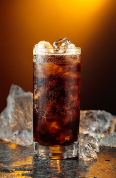 Cola with ice in misted glass on a black stone table.
