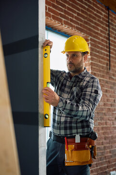 Construction worker checking wall straightness with leveling tool during home remodeling process.