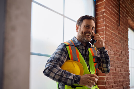 Happy construction site foreman talking on cell phone.