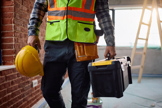 Unrecognizable worker in uniform carrying toolbox at construction site.