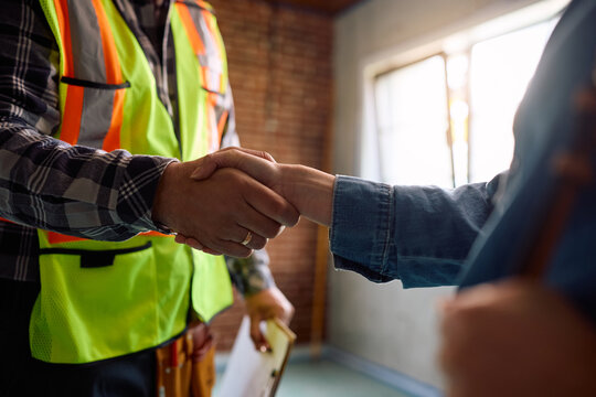 Close up of woman handshaking with building contractor at her renovating home.