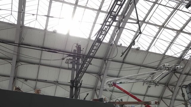 Sunlight shines through massive railway station roof above electric train cables and metal construction creating industrial transport atmosphere with engineering details