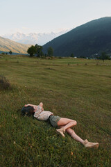 Naklejka premium Young woman lifestyle relaxing lying on grass in open field with mountains in background enjoying nature and peaceful outdoor environment on sunny day.