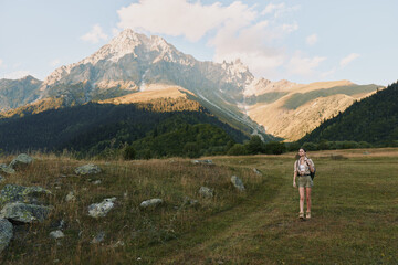 Naklejka premium Woman hiker in a mountain meadow, exploring rugged terrain with a backpack, shorts and boots, gazing at distant peaks, a calm outdoor scene with solo travel vibe.