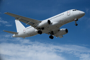 Fototapeta premium White Airplane Approaching for Landing Against Blue Sky with Clouds