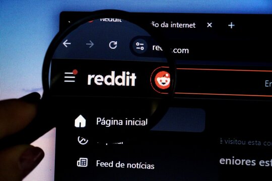 Salvador, Brazil - May 8, 2026: Reddit logo in on its Brazilian portuguese website seen through a magnifying glass. Concept of social media community. Reddit logo. 