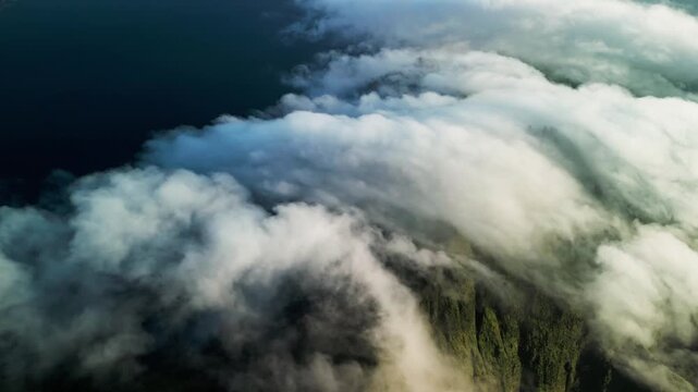 Rolling clouds over mountain ridge with fast moving cloud cover across lush green slopes creating dramatic atmospheric landscape and dynamic weather aerial drone footage