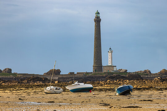 View of the Ile Vierge lighthouse with small boats resting on the sandy beach at low tide under a soft sky in Plouguerneau, Bretagne, France.