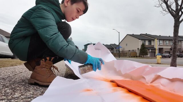 Kid spray painting his skateboard outside on front launch - close up