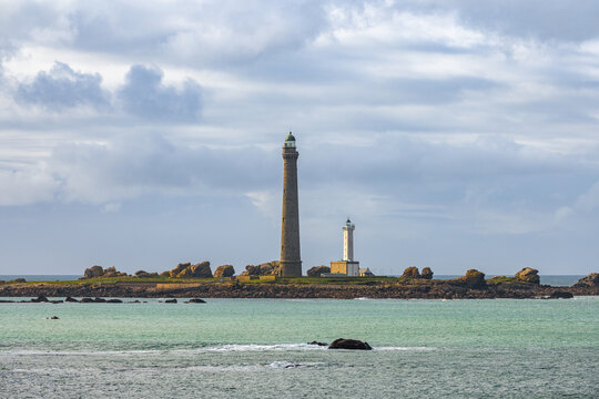 View of Ile Vierge lighthouse standing on a rocky island surrounded by turquoise sea water under a cloudy sky in Plouguerneau, Bretagne, France.