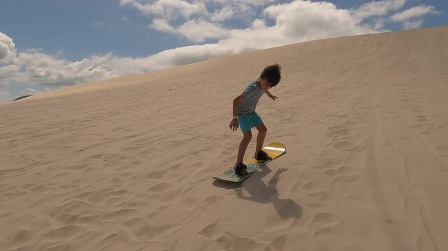 Boy struggling to slide down sand dunes on sand board - not quick enough