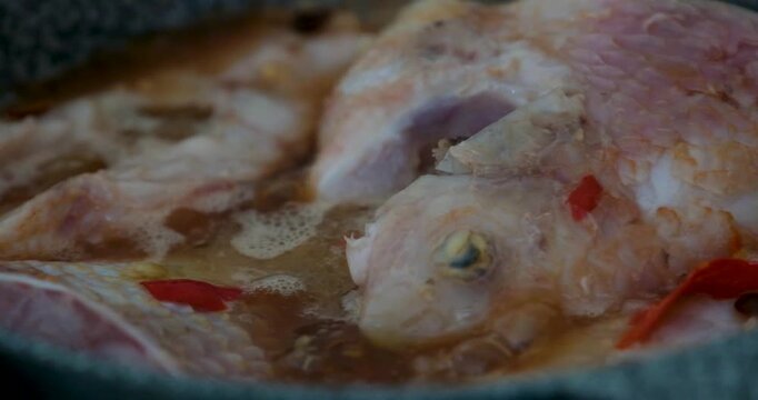 Vietnamese red fish cooking in gray pan with chili garlic and salt simmering on gas stove showing traditional soup preparation step by step