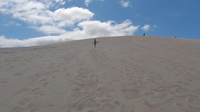 Young boy walking up sand dunes with sand board on tropical summer vacation - fun activities
