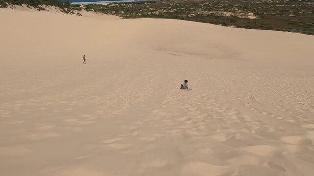 Boy sliding down sand dunes on board in tropical South America