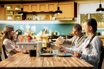 Fototapeta premium Family serving breakfast in the kitchen and pouring orange juice, enjoying eggs and pastry together. Morning routine filled with joy and love shared over meal during weekend.