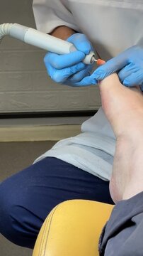 Close-up male foot receiving hardware pedicure, master technician uses diamond cutter and gloved hands to remove callus and shape
