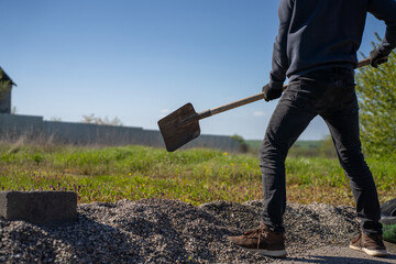 Worker with shovel stands near gravel pile on outdoor site during landscaping or construction material handling. © Marina