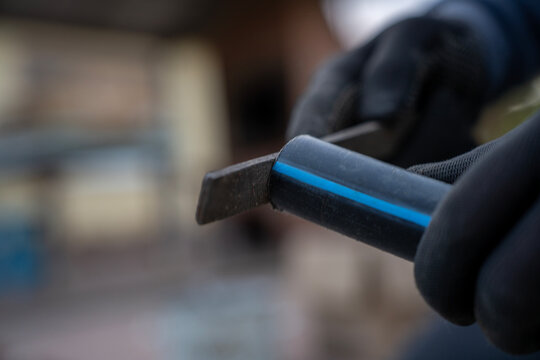 Worker in gloves smoothing the edge of a black plastic pipe with a metal file during pipe preparation.