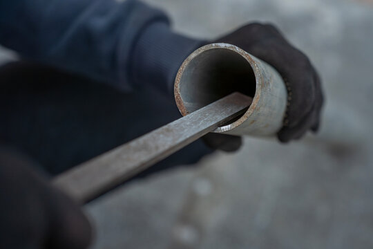 Person in black work gloves filing the edge of a metal pipe with a hand file, close-up view of manual pipe repair work.