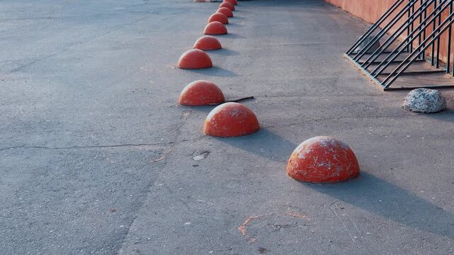 Red hemispheres lining empty pedestrian lane, bicycle rack against building wall, sunlit asphalt textures and long shadows, quiet