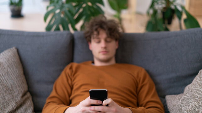 Unrecognizable Man Lying on Couch Holding Smartphone with Digital Fatigue and Passive Scrolling Concept