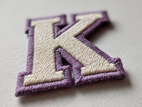 Close-up image of a 3D lavender and white stitched K letter on a white background, showcasing texture and depth Possibly intended for clothing or fabric items - AI-Generated