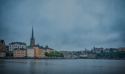 Fototapeta premium Stockholm Sweden Waterfront Skyline with Riddarholmen Church Historic Buildings and Bridges Under Overcast Sky Across Calm Water