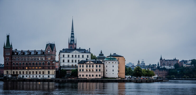 Stockholm Sweden Riddarholmen Waterfront Skyline with Historic Buildings and Church Spire Reflected in Calm Water Under Overcast Sky