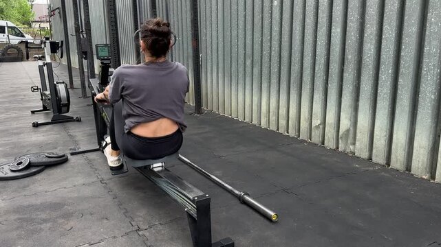 Woman training on rowing machine in outdoor gym with calisthenics equipment, fitness endurance workout, active lifestyle, strength training and healthy routine.
