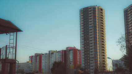 Modern high-rise apartment building towering over colorful old panel houses under a clear blue sky, urban development and architectural contrast in a residential district. © Вита Курило