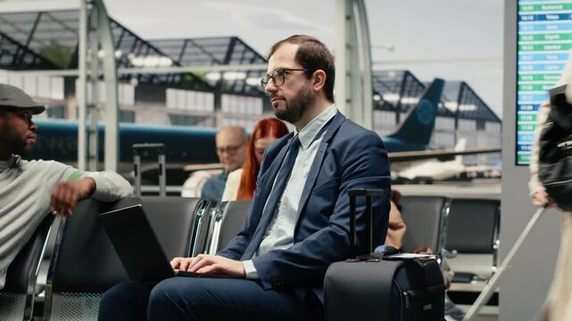 Freelancing man in airport looking at plane departure timetable using laptop during business trip. Businessman doing travel destination itinerary, typing on notebook keyboard, camera A