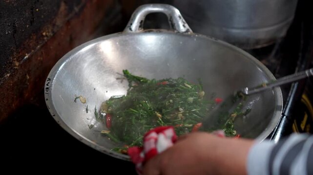 A vendor cooks stir-fried bracken for customers. Indonesian street food.