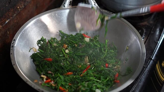 A vendor cooks stir-fried bracken for customers. Indonesian street food.