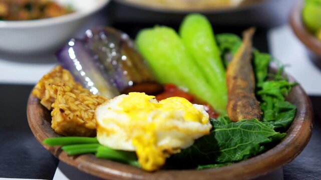 Indonesian spicy (sambal) on an earthenware plate with fried eggplant, fried tempeh, fried salted fish and chayote.