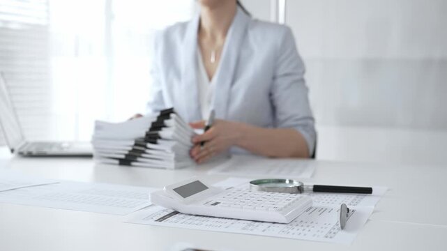 Business person working on financial documents, accounting or auditing a large stack of paperwork, managing tax forms and corporate reports with a pen at an office desk. Audit and taxes