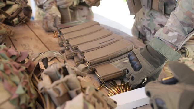 A group of men in military uniforms are loading machine gun magazines with cartridges.