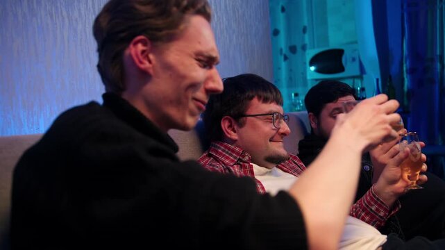 Joyful friends share lively celebration and toast joyfully. Three smiling young caucasian men laugh, hold glasses, clink and drink cognac in cozy living room ambiance. The harm of alcohol consumption