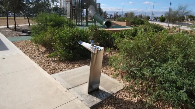 A modern stainless steel drinking fountain with a water bubbler in a public park, near a children's playground in Truganina, Melbourne Australia. Family-friendly amenities and recreational facility