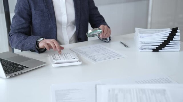 Professional accountant reviewing financial documents and using calculator and laptop to verify figures for audit compliance. Audit and taxes
