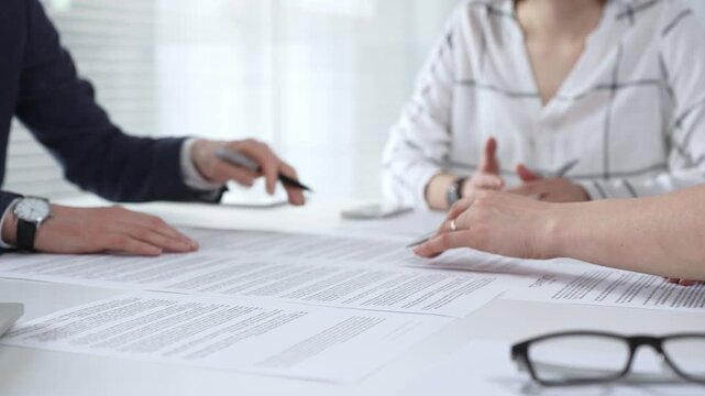 Business people discussing contract documents on a white desk, analyzing clauses and terms during an office meeting, collaborating on important paperwork for agreement